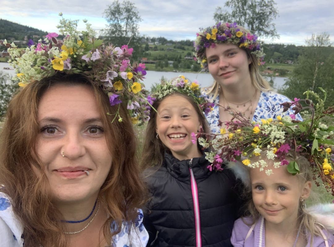 A mother and her three daughters in handmade flower crowns, by a lake on a summer evening