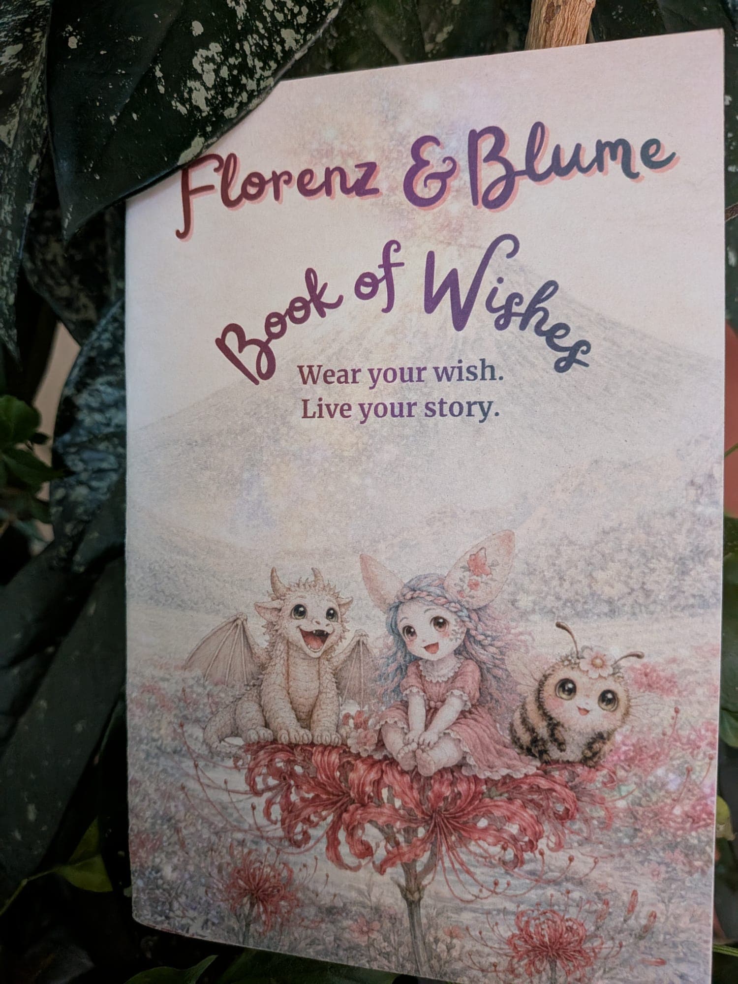 The Book of Wishes cover — Florenz, Blume and Pim on a spider lily, under the words "Wear your wish. Live your story."