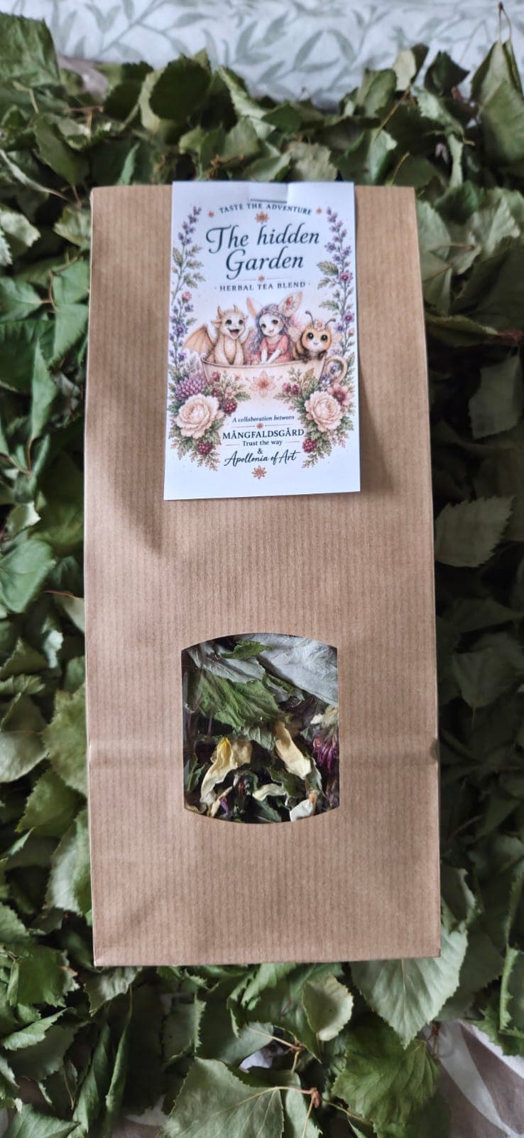 The Hidden Garden herbal tea blend in a kraft bag with a window, lying on dried leaves