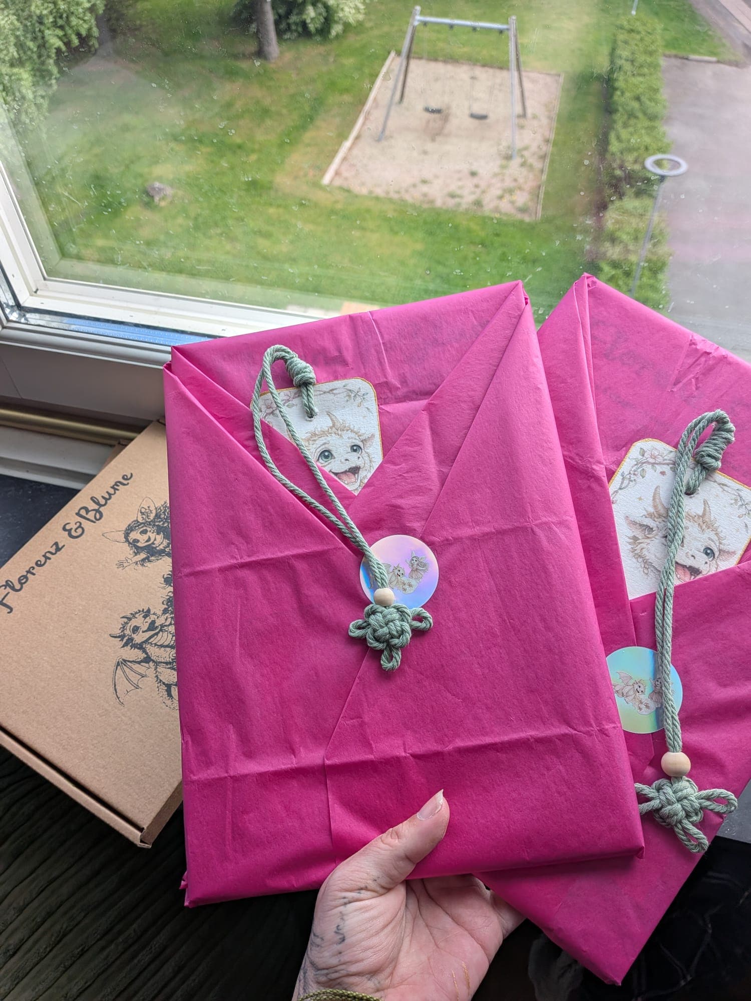 Two sets wrapped in pink tissue, each tied with a green cord and a hand-painted dragon tag, held up at a window