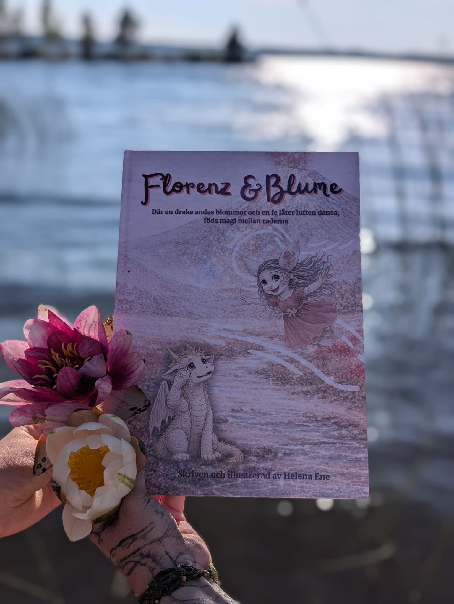 The hardcover held up by the lake with a water lily and a dahlia