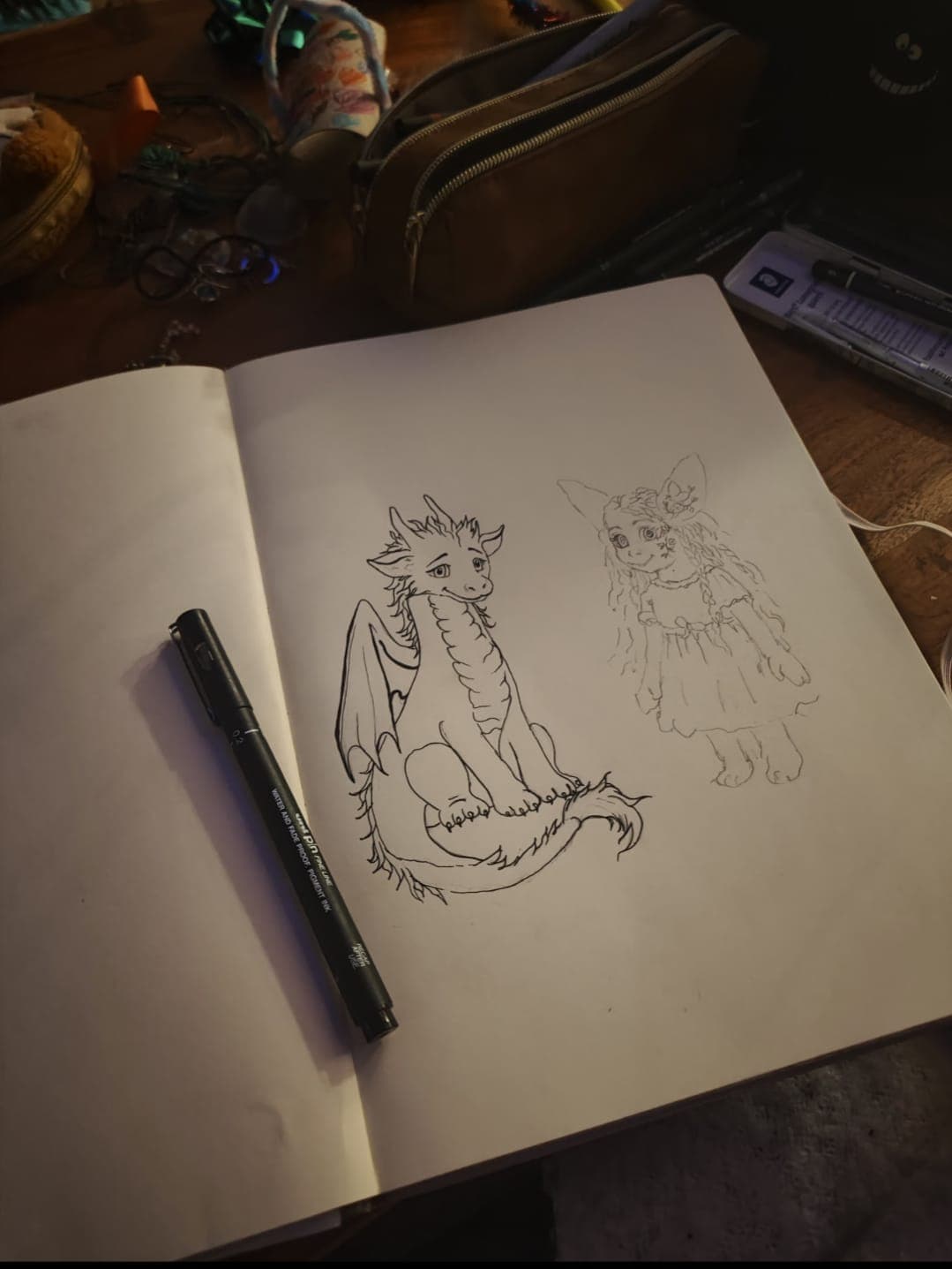 Ink sketches of Florenz and Blume on an open sketchbook, on a cluttered desk at night