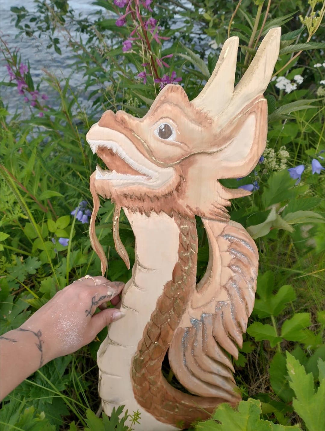 A hand-carved wooden Florenz held up among wildflowers by the water